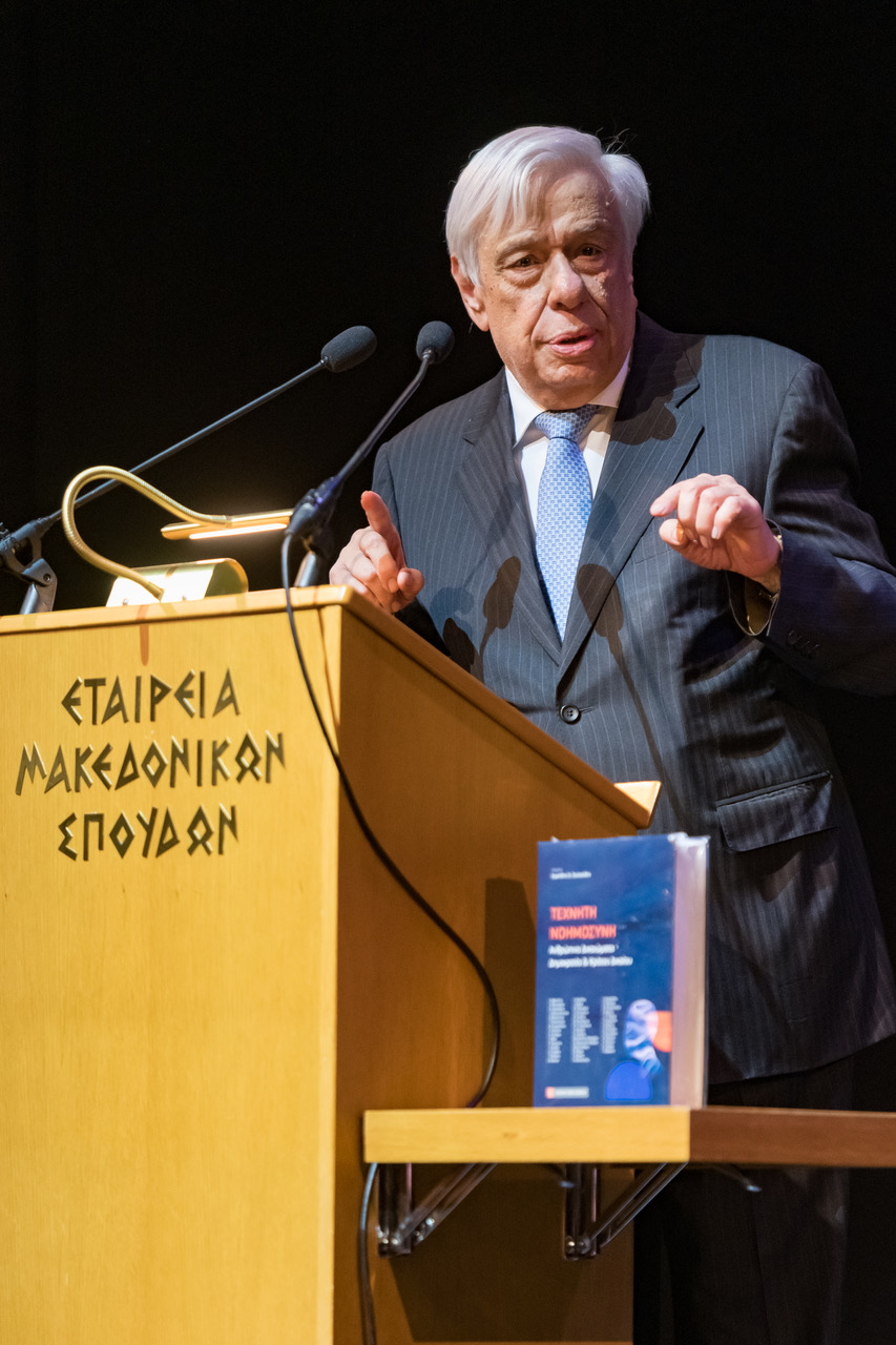 Ομιλητής στο αναλόγιο με μικρόφωνα και βιβλίο στο προσκήνιο.