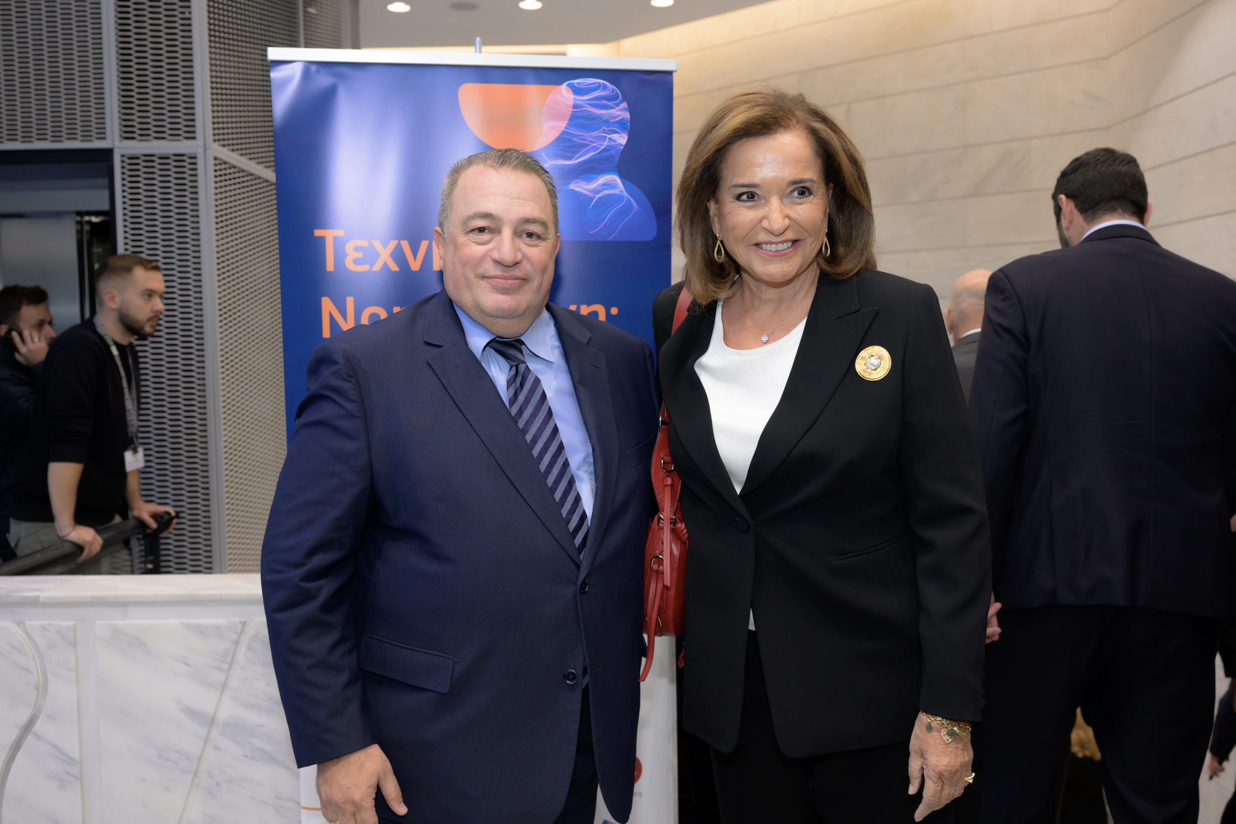 Δύο άτομα φωτογραφίζονται μπροστά από το πανό της εκδήλωσης.