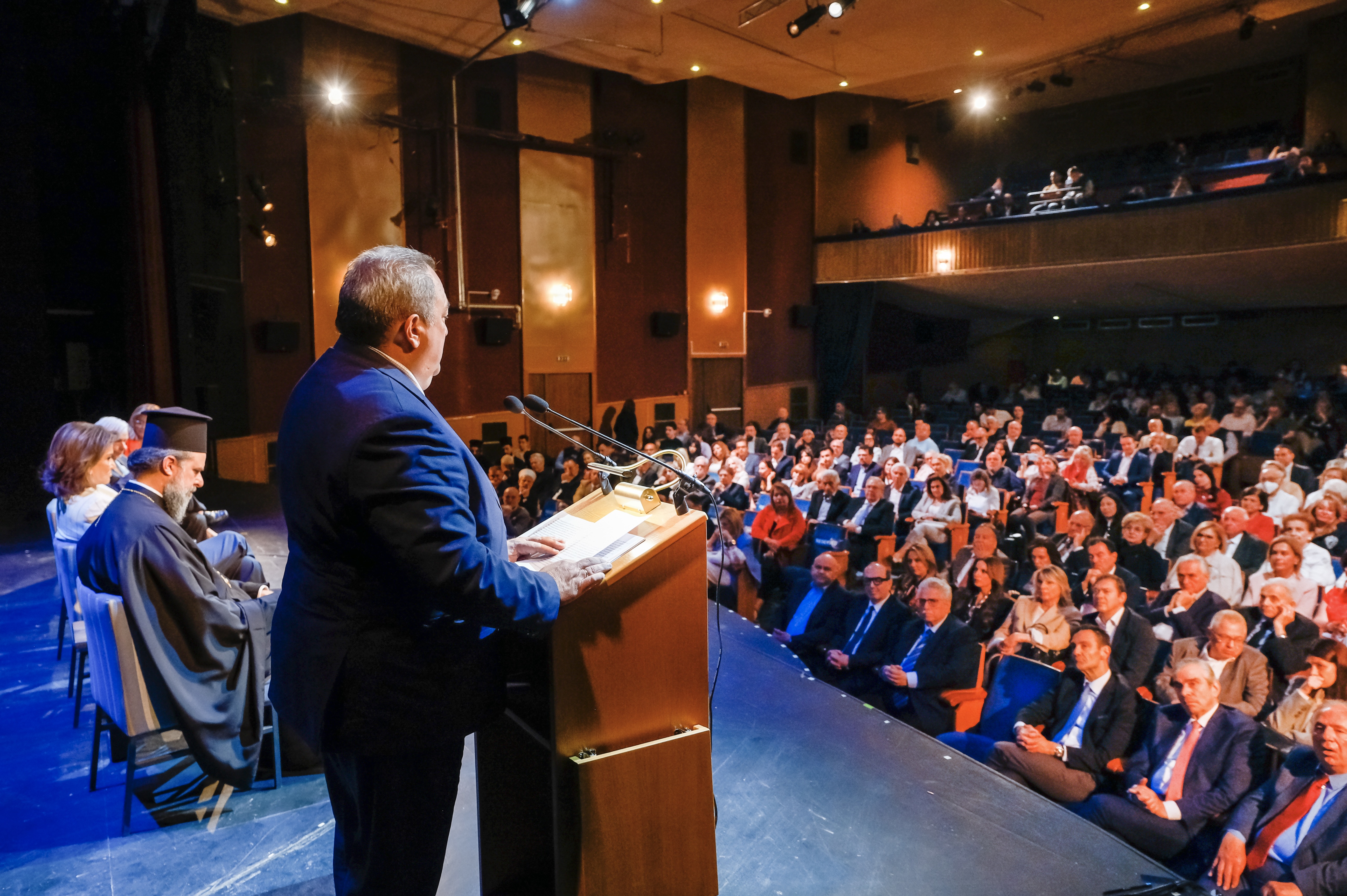 Ομιλητής στο αναλόγιο και γενική άποψη του κοινού από το πλάι της σκηνής.